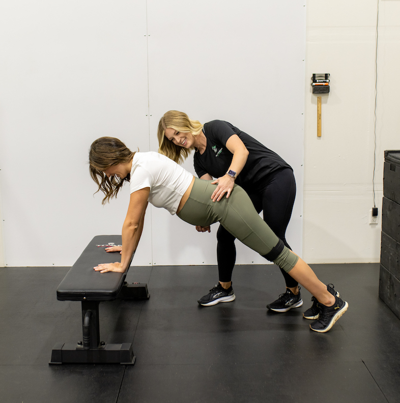 Two women doing squats on a bench.
