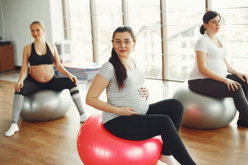 Three pregnant women sitting on exercise balls in a gym.