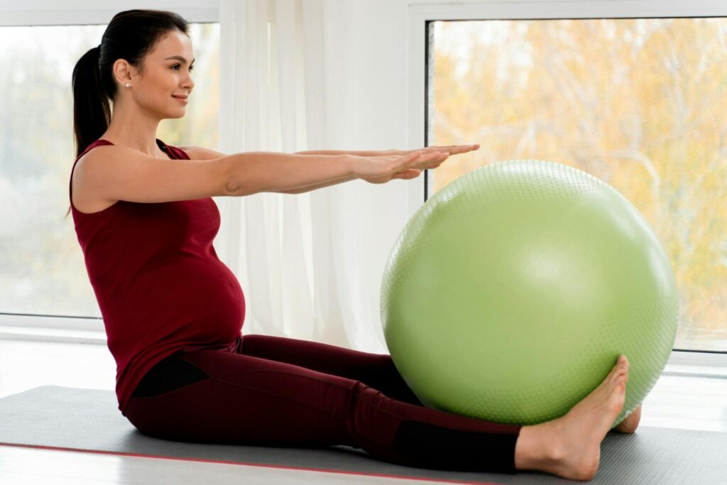 A pregnant woman doing yoga with a green exercise ball.